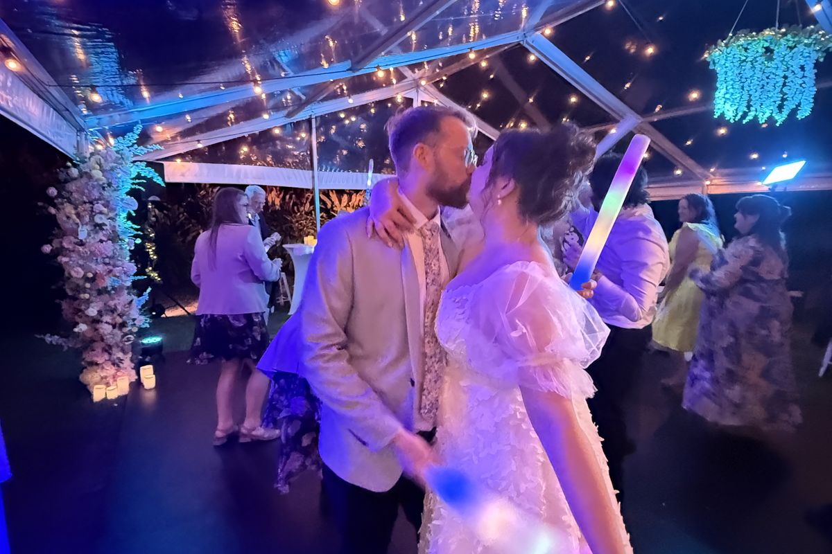 Couple under festoon lights inside a clear-roof wedding marquee