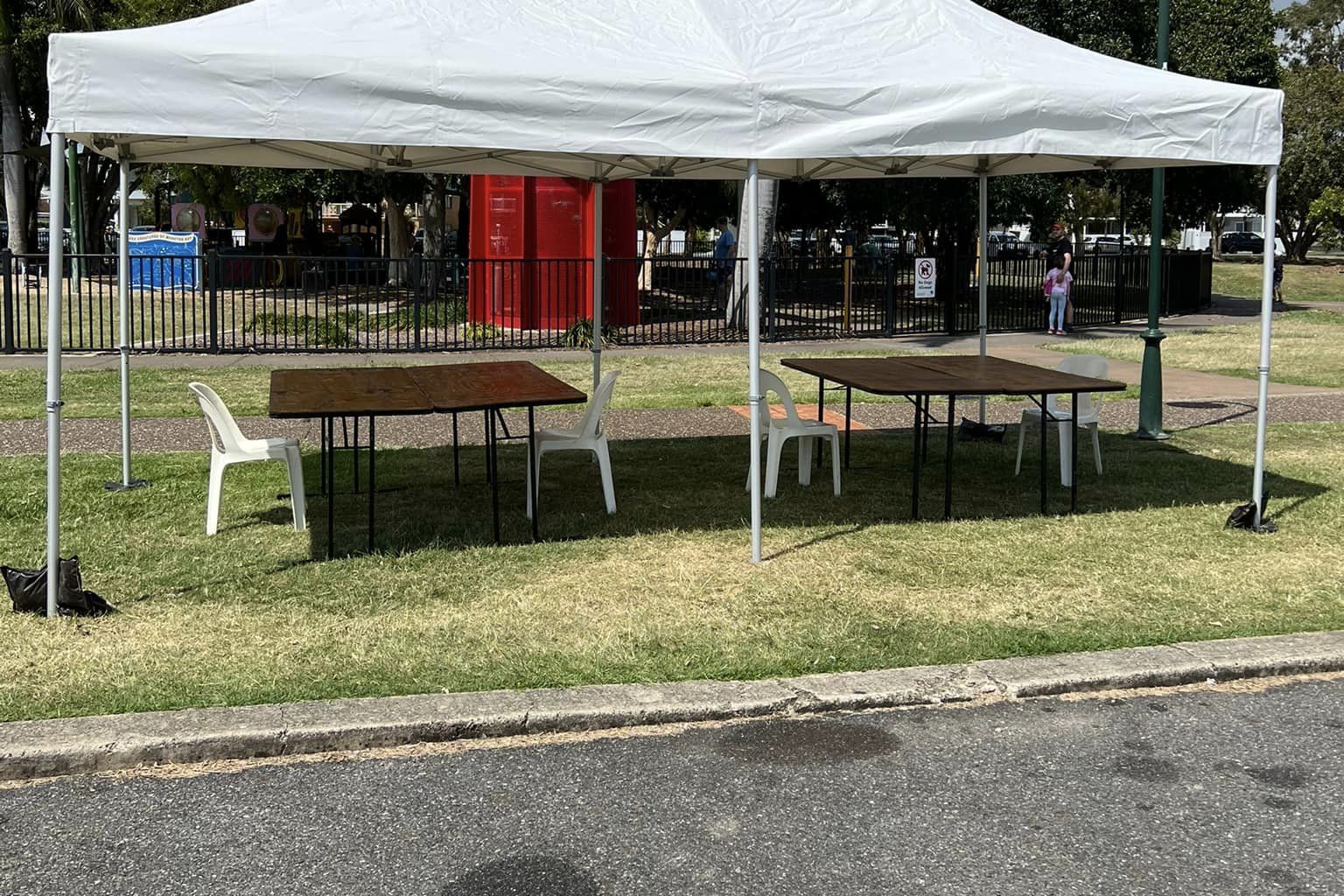White pop-up gazebo over timber tables beside a park